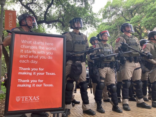 Auto-generated description: A group of riot police officers in full gear stands next to a sign with a motivational message, likely at a public event or demonstration.